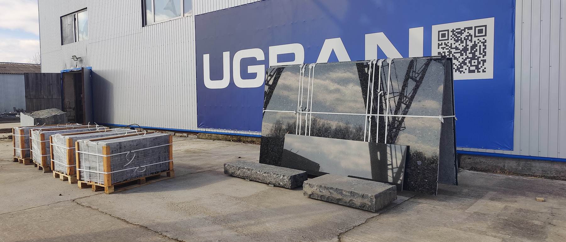 UGRAN plant yard: slabs, pallets and the workshop with the company banner